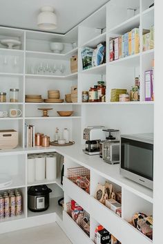 a kitchen with white shelving and lots of food on the counter top in front of a microwave