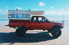 a red pick up truck with a camper on the back parked at the beach