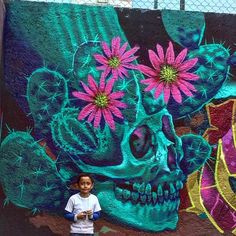 a young boy standing in front of a colorful wall with a skull and flowers painted on it