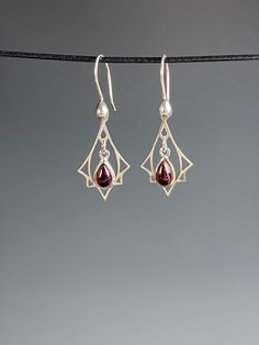 "Art Deco lovers rejoice! Here are red Garnet earrings in Sterling silver! So often we see Art Deco designs that are only red and gold but I also make Garnet and silver jewelry in Art Deco inspired designs. These sweet earrings are lightweight and easy to wear. The deep red Garnet gemstones smooth cabachons that are bezel set in Sterling silver that dangle freely in a Sterling Art Deco charm. They hang 1.5 inches on Sterling silver ear wires with a sterling accent. These also make a wonderful gi Elegant Artistic Drop Earrings, Elegant Artistic Design Drop Earrings, Elegant Artistic Drop Earrings Jewelry, Sterling Silver Teardrop Jewelry With Artistic Design, Artistic Sterling Silver Teardrop Earrings, Elegant Sterling Silver Jewelry With Artistic Design, Artistic Dangle Jewelry As Gift, Artistic Dangle Jewelry For Gifts, Artistic Design Dangle Jewelry Gift