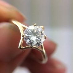 a person holding a ring with a white diamond in it's center and gold band