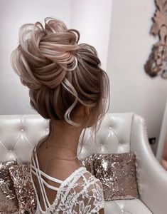 a woman sitting on top of a white couch wearing a dress and hair in a low bun