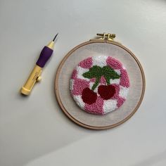 a small embroidered object with a needle and thread next to it on a white surface