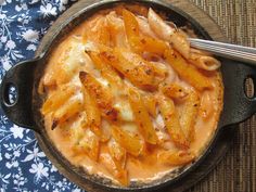 a skillet filled with pasta and sauce on top of a blue floral cloth next to a spoon