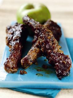 two pieces of meat sitting on top of a blue plate next to green apple slices