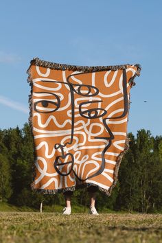 an orange and white blanket with black writing on it in front of green grass, trees