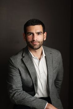 a man in a gray jacket and white shirt is posing for a photo with his arms crossed