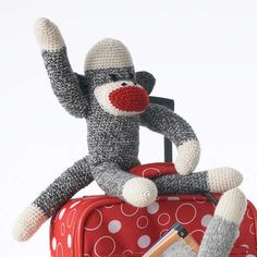 a stuffed monkey sitting on top of a red suitcase with its arms in the air