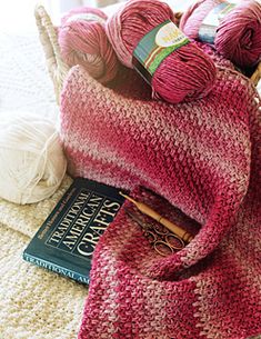 a basket filled with balls of yarn sitting on top of a bed next to a book