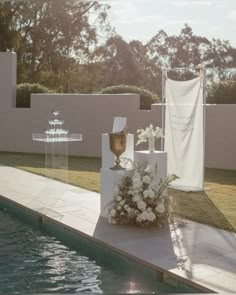 an outdoor ceremony setup with flowers and vases on the side of a pool in front of a white fence