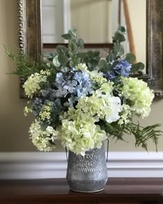 a vase filled with blue and white flowers on top of a wooden table next to a mirror