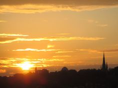 the sun is setting over a city with tall buildings and spires in the background