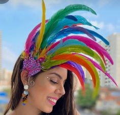 a woman in a colorful dress and headdress smiles at the camera while standing on a balcony