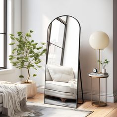 a mirror sitting on top of a wooden floor next to a white couch and potted plant