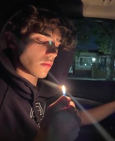 a young man holding a lit candle in his hand while sitting in the back seat of a car