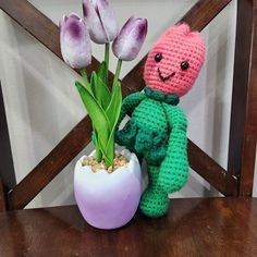 a crocheted stuffed animal sitting next to a potted plant with purple tulips