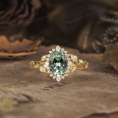 a ring with an oval cut green and white diamond surrounded by leaves on the ground