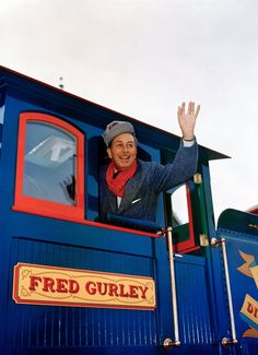 a man waving from the top of a blue train caboose with his hand in the air