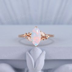 a white opal and diamond ring sitting on top of a white cloth covered box