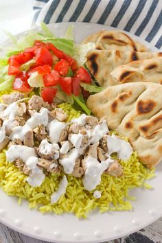 a white plate topped with rice, chicken and veggies next to pita bread