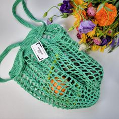 a green crochet bag next to a bouquet of flowers on a white surface