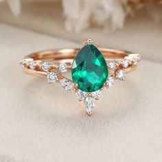 a ring with an emerald colored stone and white diamonds on it, sitting next to a flower