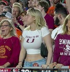 two women are sitting in the stands at a football game and one woman is holding her hand up