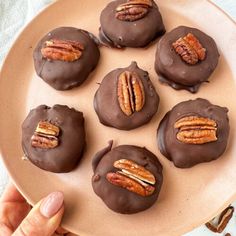 chocolate covered donuts with pecans in the middle on a plate, being held by a person