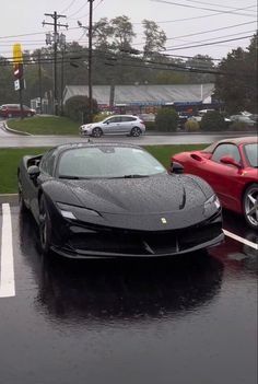 two ferraris parked in a parking lot on a rainy day, one is red and the other is black