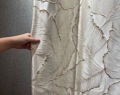 a person is holding up a curtain with white feathers on it and the fabric has been drawn