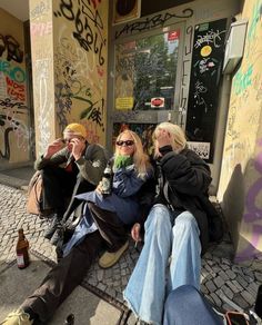 three people are sitting on the sidewalk with their feet up and one is holding a beer