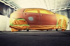 an orange car covered in yellow tarp sitting on top of a parking garage floor