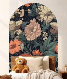 a teddy bear sitting on top of a bed in front of a floral wallpaper