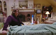 a woman sitting in a living room next to a bed with a blanket on it