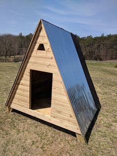 a small wooden structure with a metal roof in the middle of a grassy field next to trees