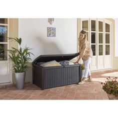 a woman standing next to an open storage box on the ground near a potted plant