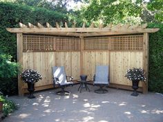 two chairs are sitting in front of a wooden privacy wall with potted plants on either side