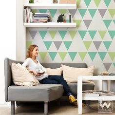 a woman sitting on a couch in front of a wall with triangles painted on it