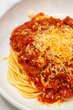 a white plate topped with spaghetti covered in sauce and parmesan cheese on top