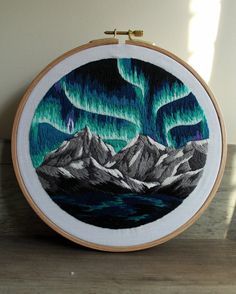 an embroidery project with mountains and the aurora lights in the sky, on a wooden table