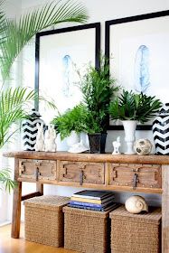 a wooden table topped with baskets filled with plants and potted plants next to two framed pictures