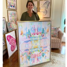 a woman holding up a large painting in front of some framed pictures and paintings on the wall