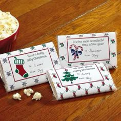 three candy bar wrappers sitting on top of a wooden table next to a bowl of popcorn