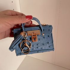 a hand holding a small blue purse with a gold ring on the handle and keychain attached to it