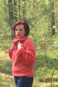 a woman standing in the woods with her hands on her hips and wearing a red sweater