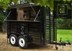 an old fashioned bar cart is parked on the grass in front of some trees and bushes