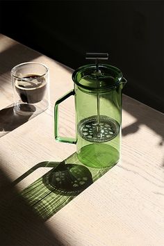 a green coffee pot sitting on top of a wooden table next to a glass cup