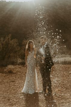 a bride and groom standing in the middle of an open field with water splashing on them