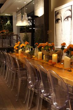 a long wooden table with clear chairs and vases filled with orange flowers on it