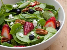 a salad with spinach, strawberries and blueberries in it